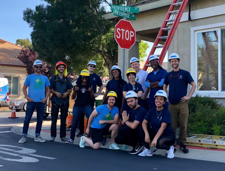 Blue State's Oakland team and Grid Alternatives client posing in front of stop sign