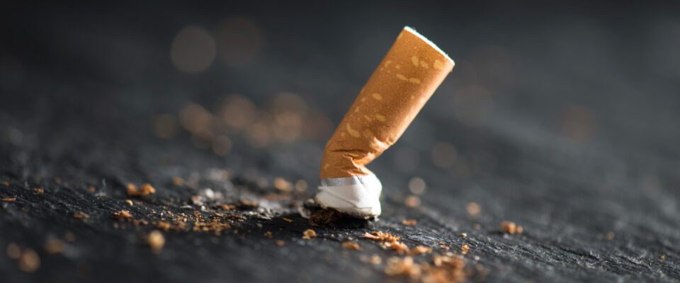 Close up photo of a cigarette butt on dark asphalt